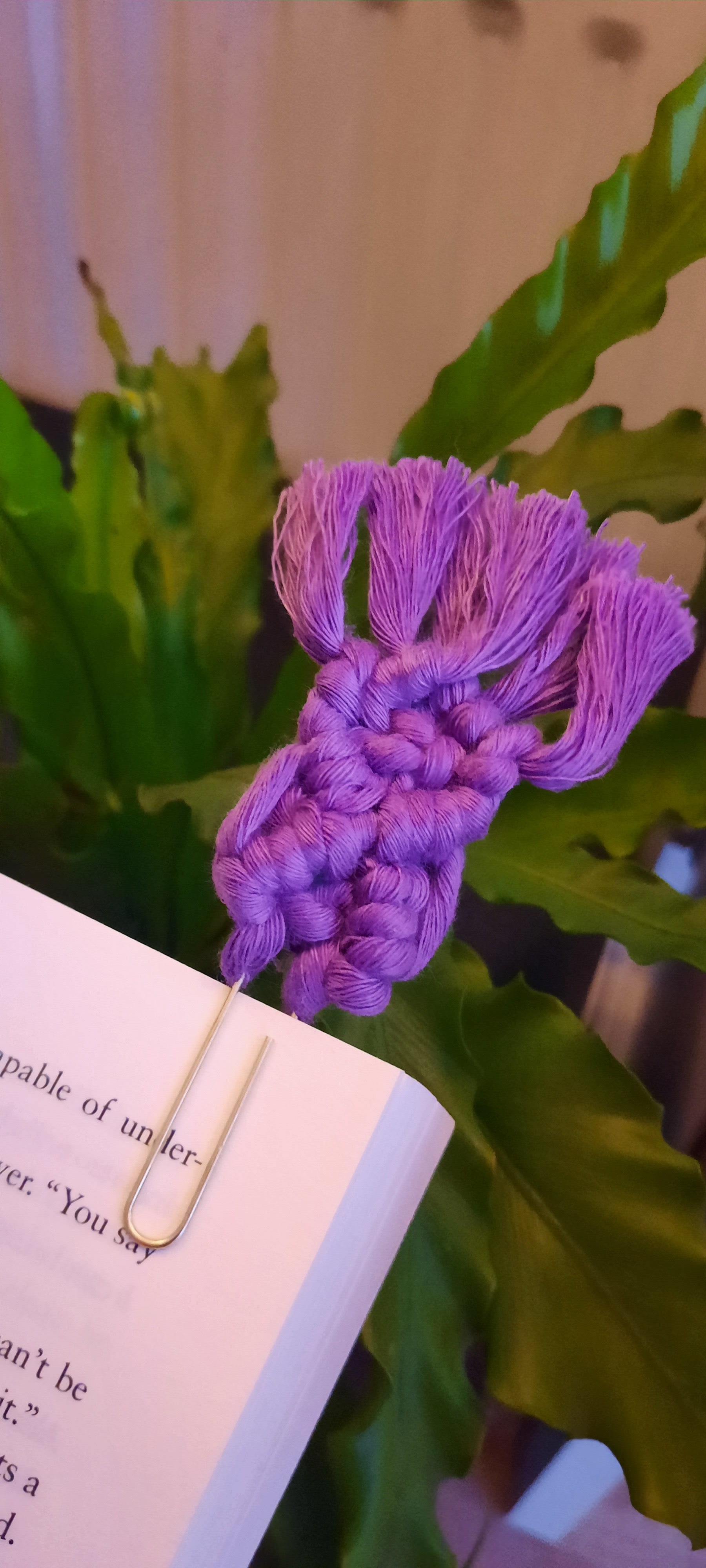 Purple braided bookmark on a book with green leaves in the background