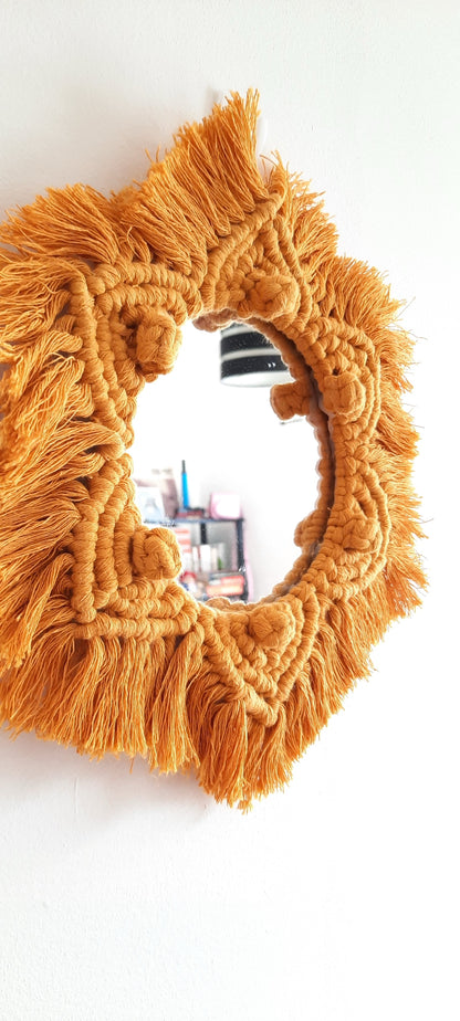 Round mirror with orange macrame frame on a white background