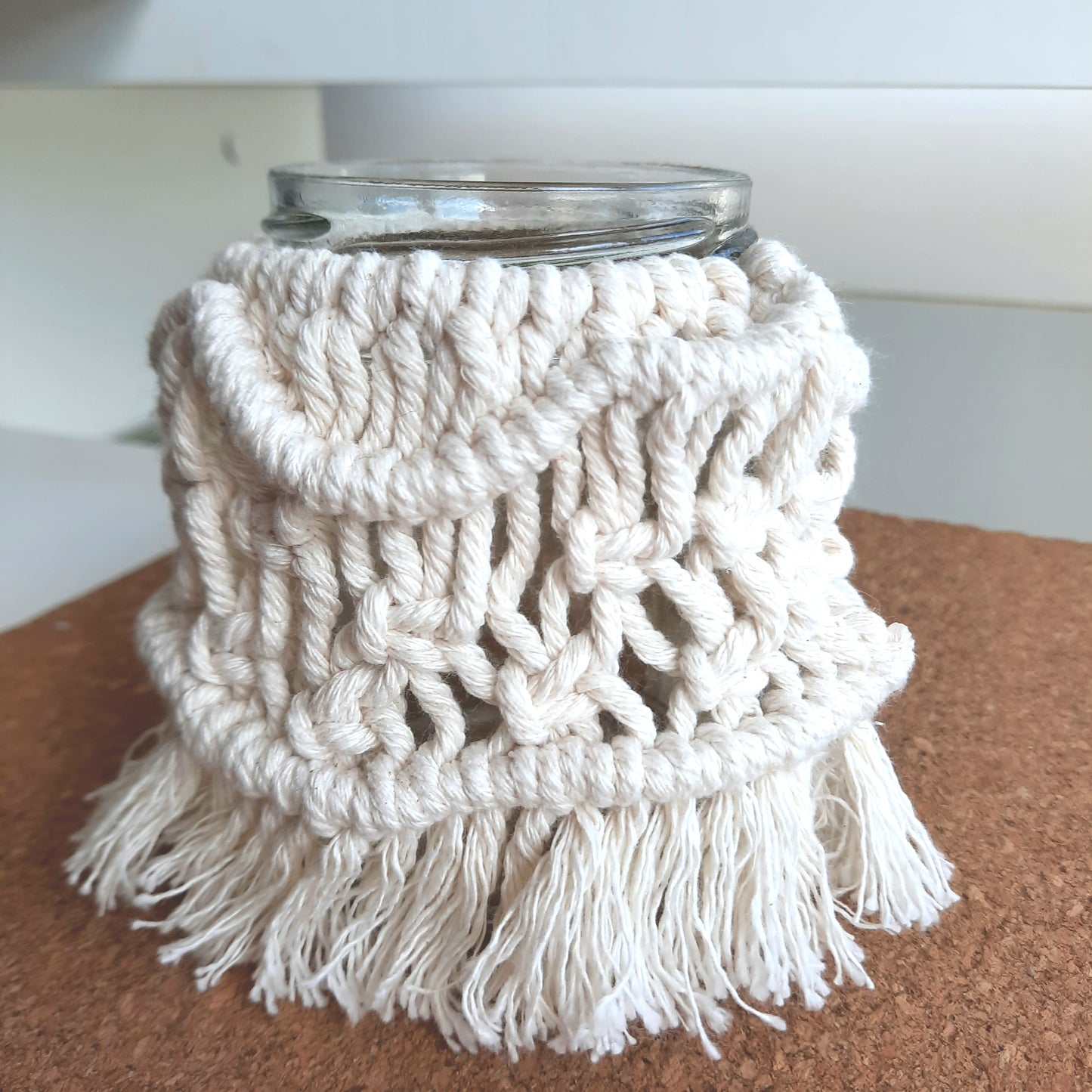 Macrame-wrapped glass jar on a wooden surface with a white background