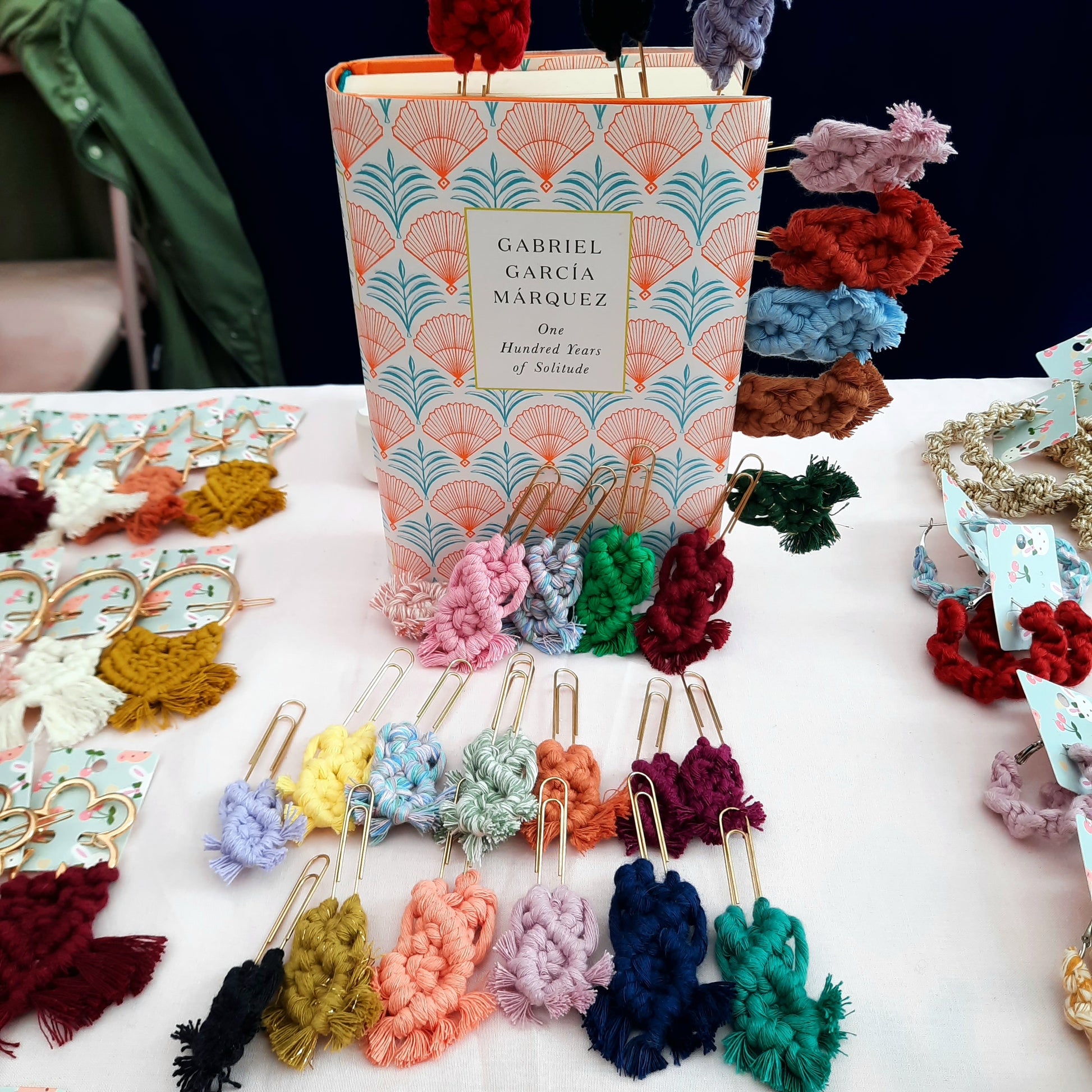 Colorful yarn-wrapped bookmarks displayed on a table with a book titled 'One Hundred Years of Solitude' by Gabriel Garcia Marquez.