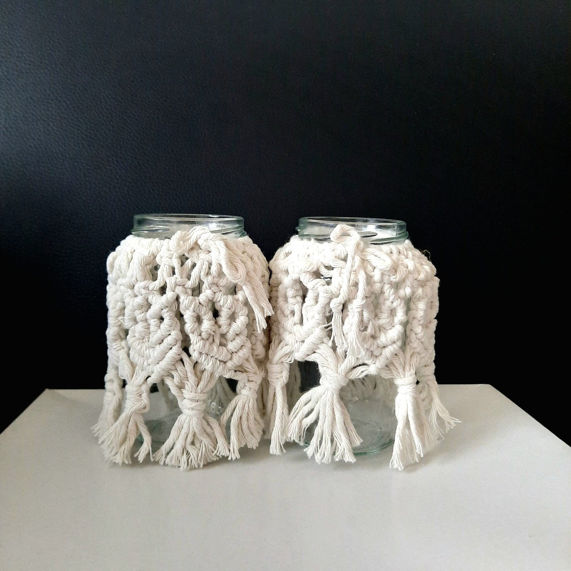 Two glass jars with white knitted covers on a black background