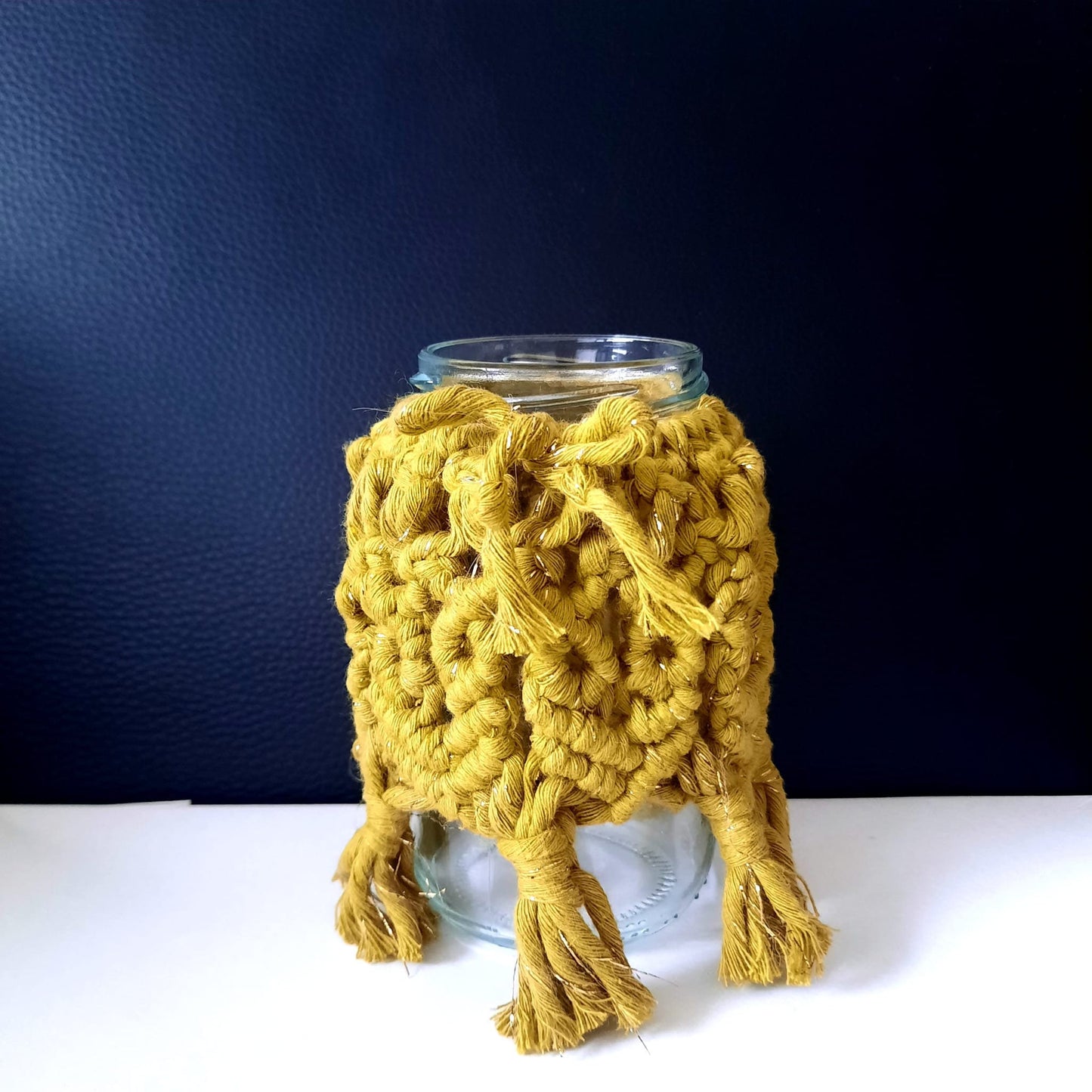 Glass jar with a yellow knitted cozy on a dark blue background