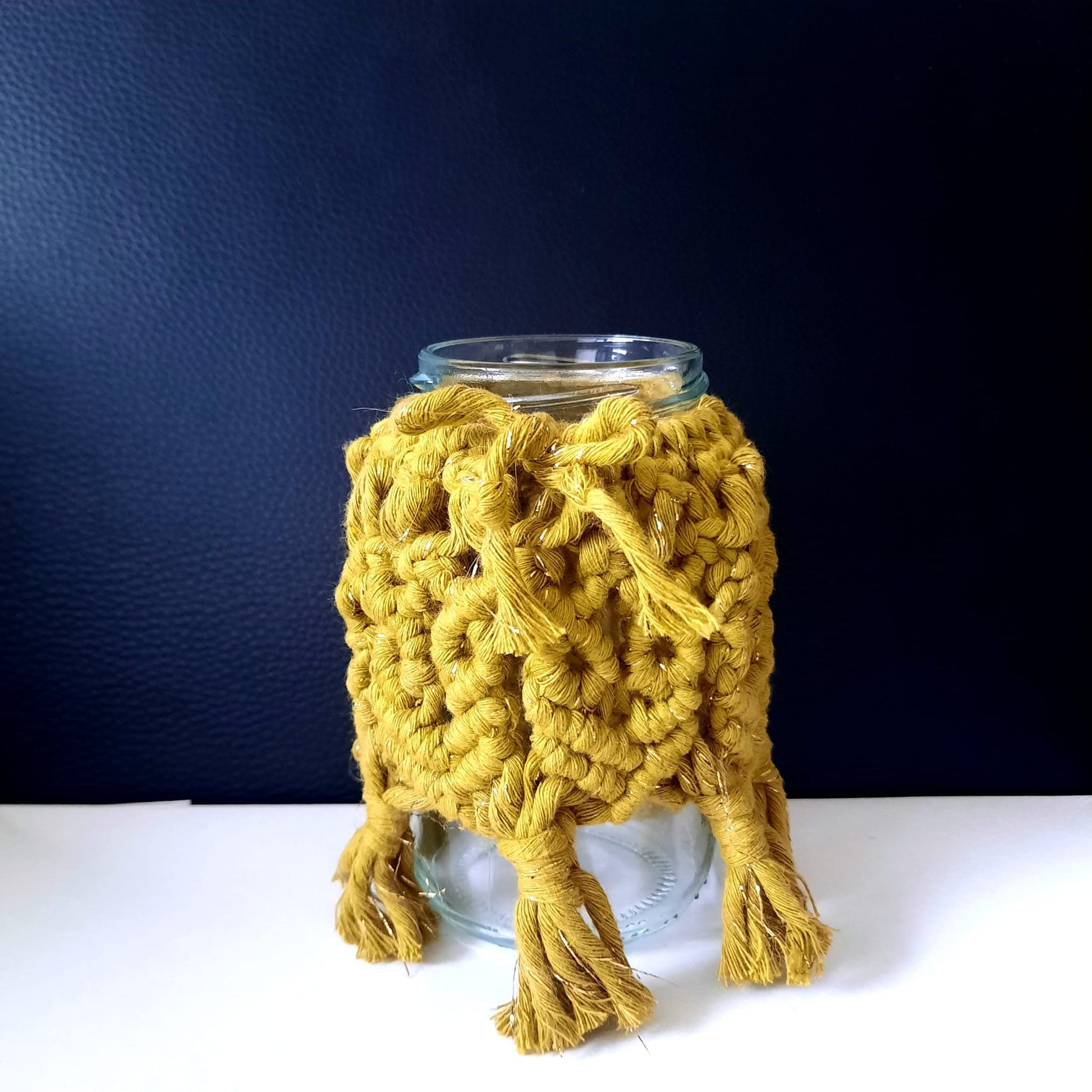 Glass jar with a yellow knitted cozy on a dark blue background