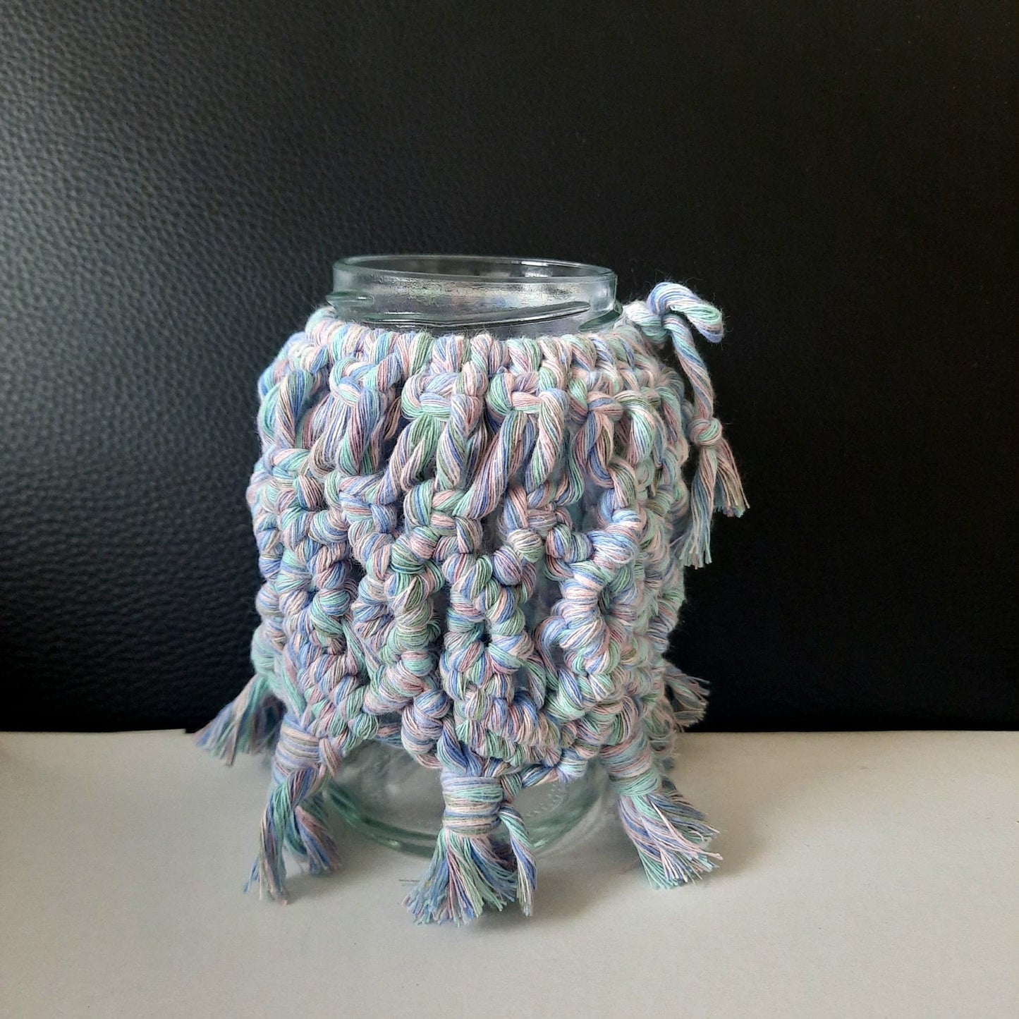 Glass jar with a colorful knitted cozy on a black background