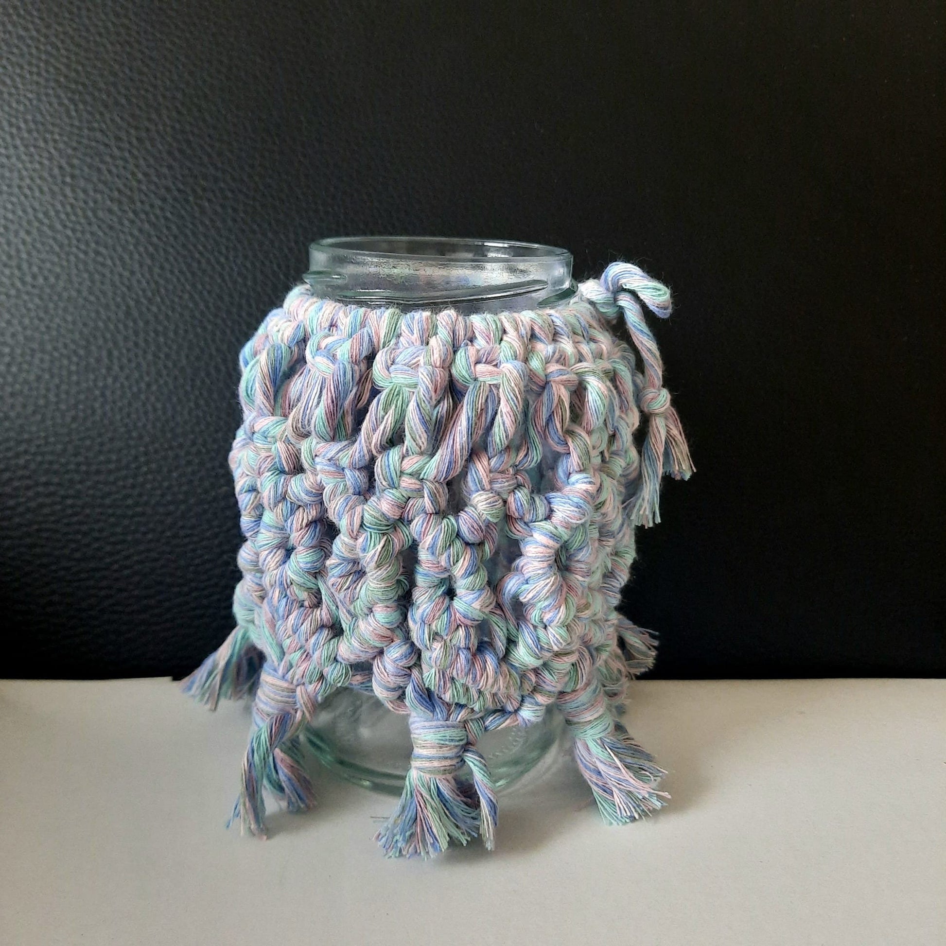 Glass jar with a colorful knitted cozy on a black background