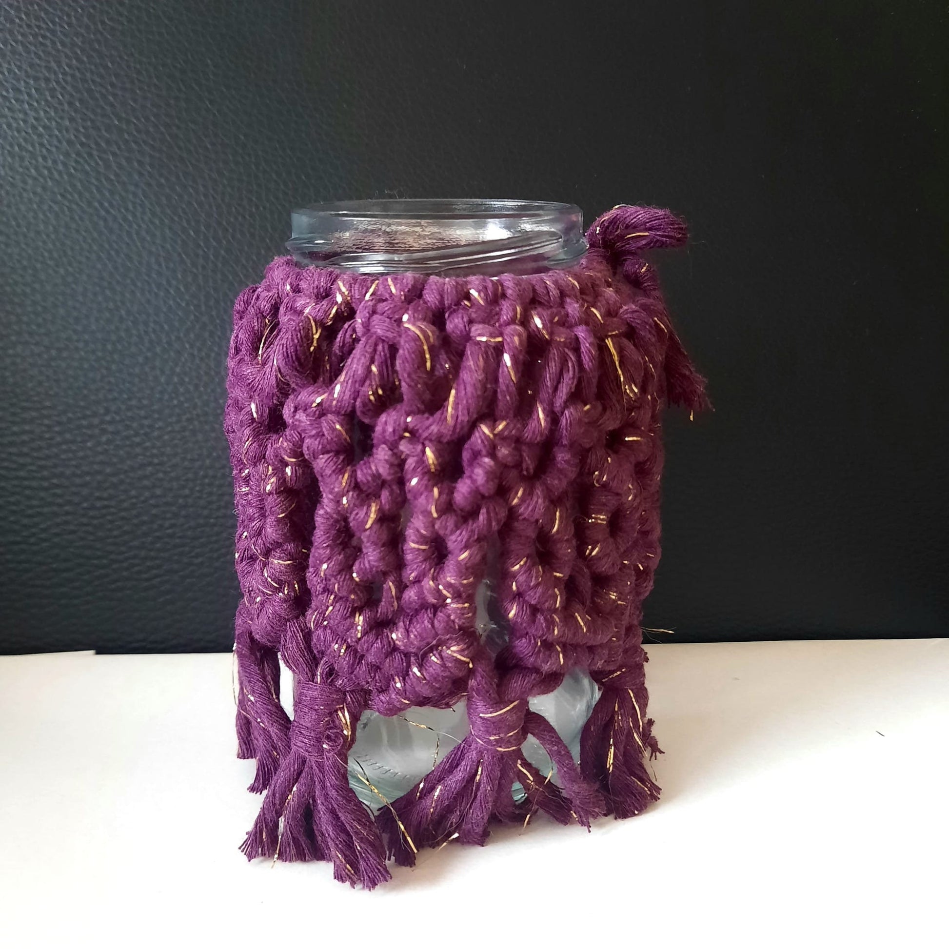 Glass jar with a purple knitted cozy on a white surface against a dark background