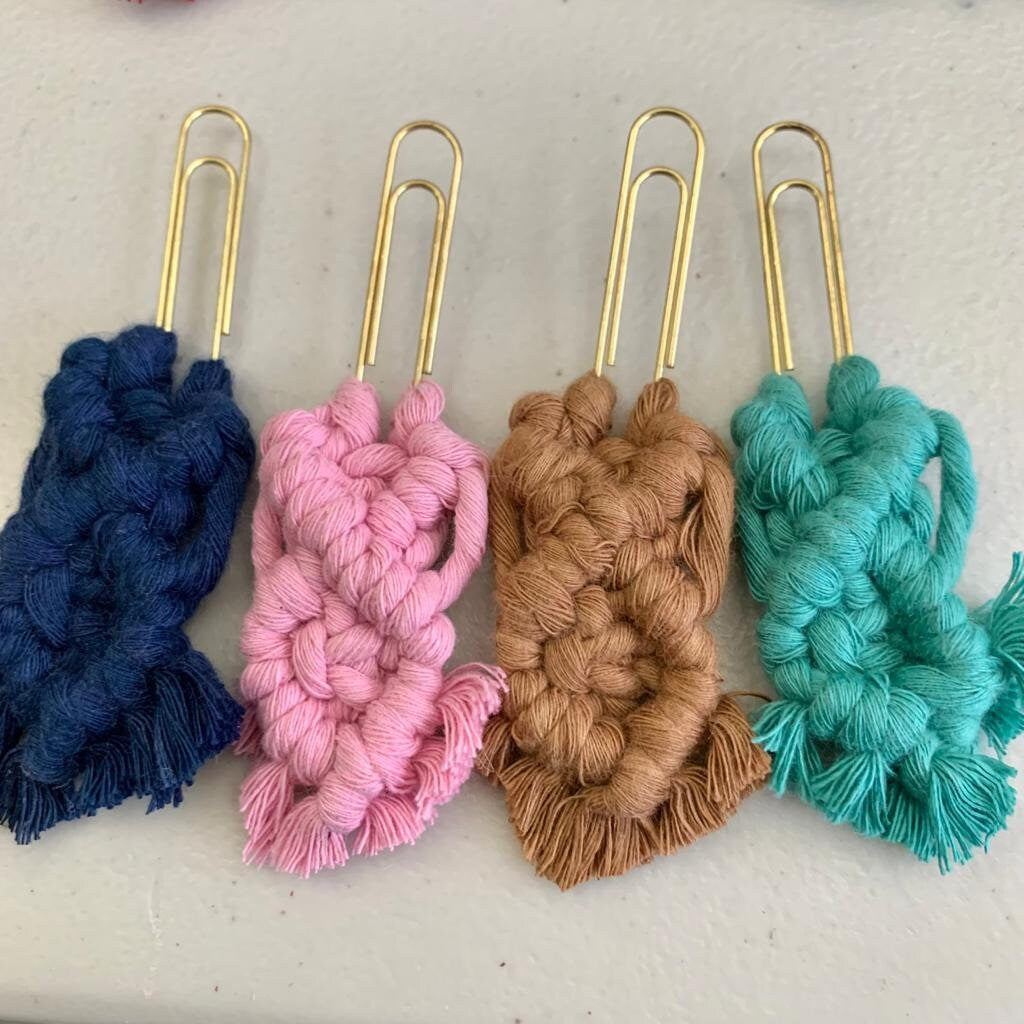 Four paperclips with knotted yarn in blue, pink, brown, and green on a light background