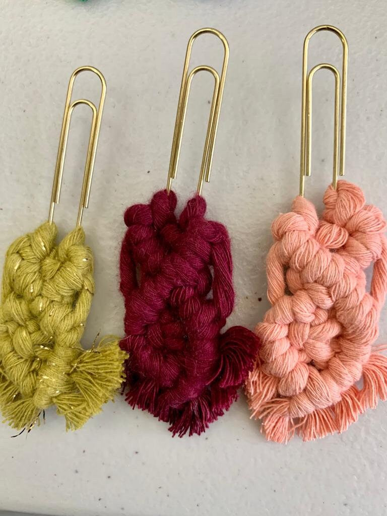 Three yarn clippies bookmarks in yellow, red, and pink on a light gray background