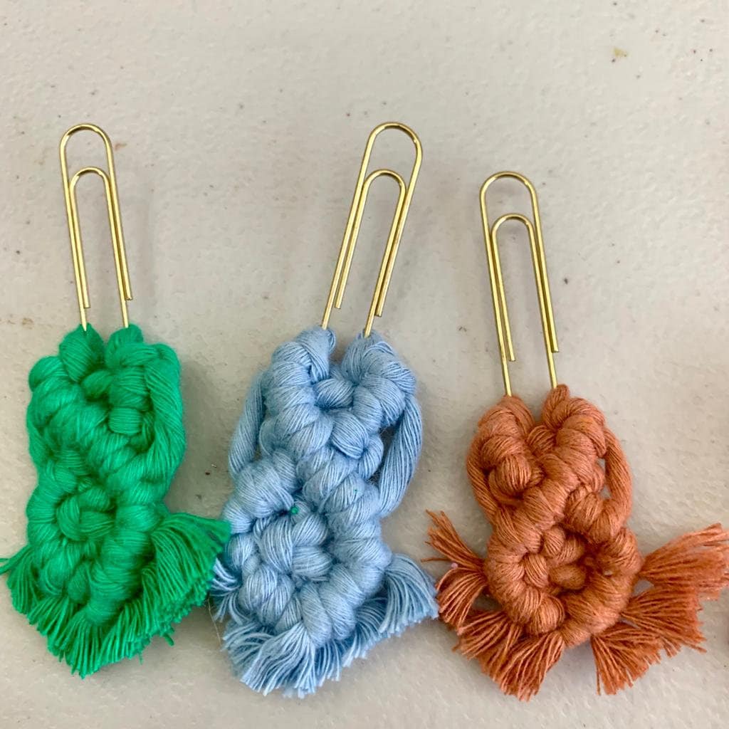 Three decorative paper clip bookmarks with braided yarn in green, blue, and orange on a beige background.