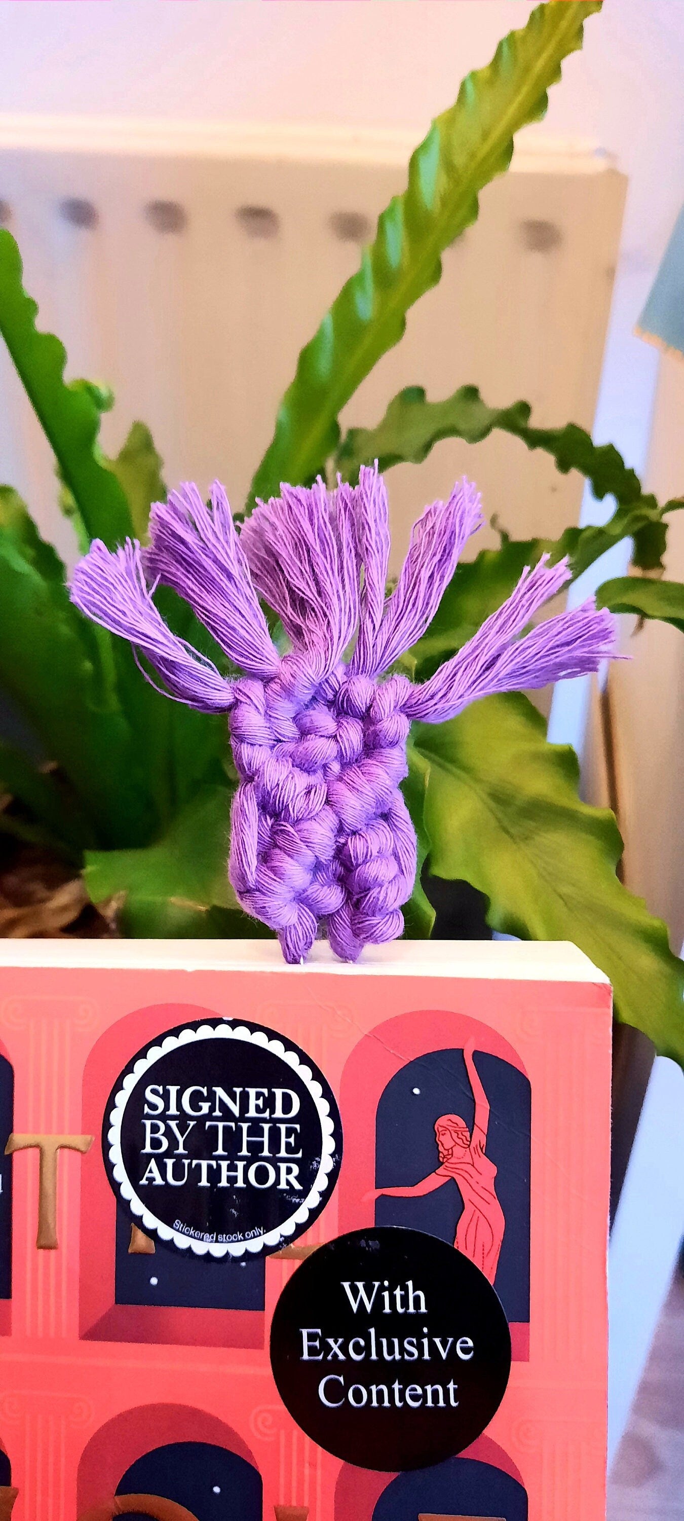 Book with a purple bookmark paperclip on top, set against a green plant background